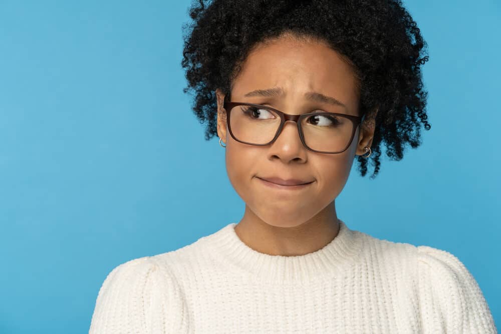 African American female wearing brown glasses and small gold earrings with naturally curly 4c coil hair.