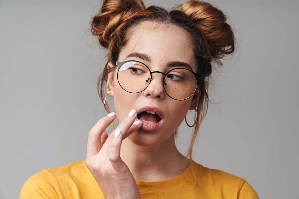 Fashion-conscious young woman with freckles and blue eyes, wearing black round glasses and pink lipstick with short natural hair and a straight uniform curl pattern.