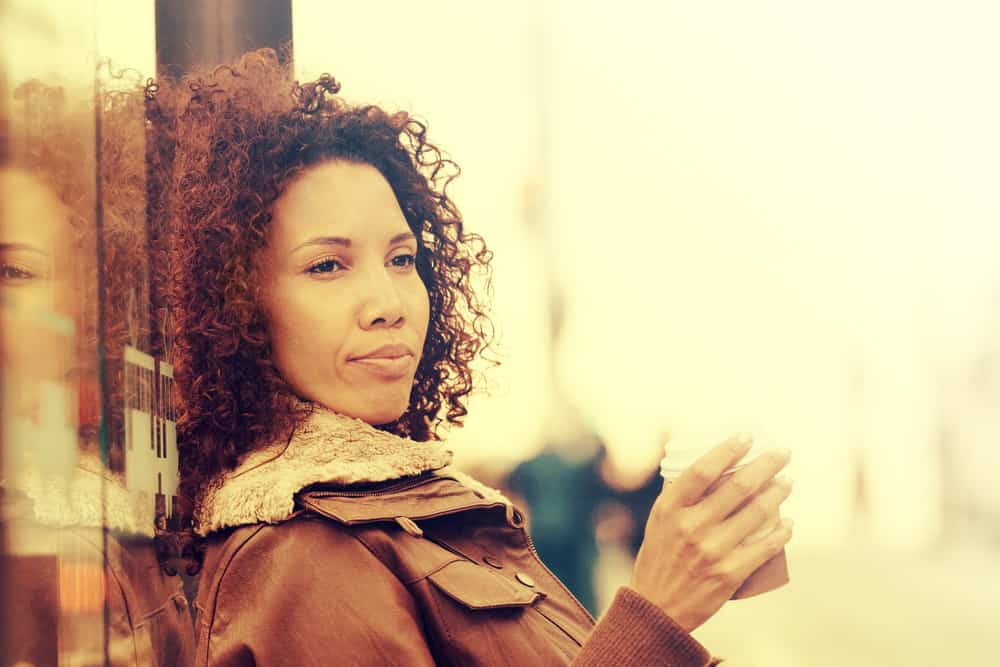  sort pige med naturligt krøllet hår iført en brun frakke og drikker te.