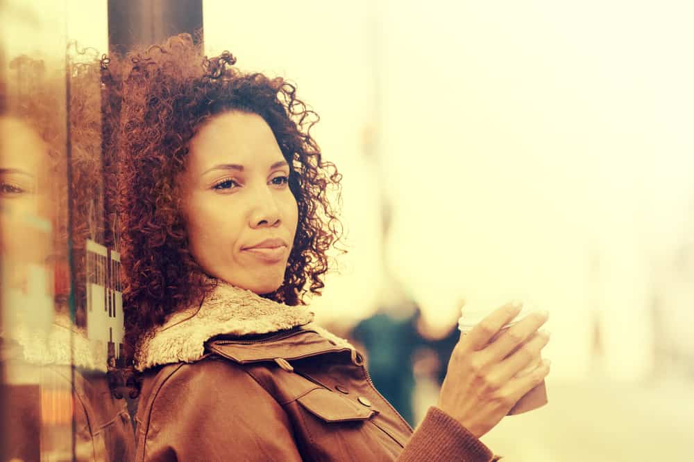  Fille noire aux cheveux naturellement bouclés portant un manteau brun et buvant du thé.