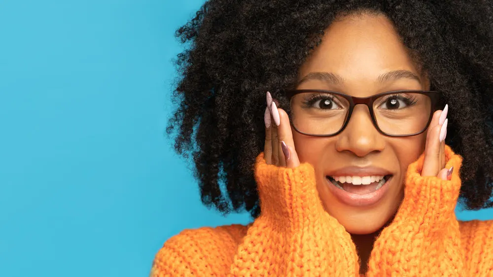 Excited black girl with curly hair wearing an orange sweater and peach fingernail polish.