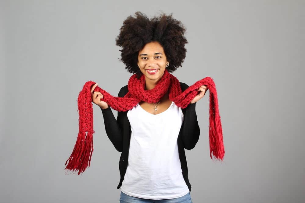 African American female wearing black pearl earrings, a silver necklace, red scarf, white t-shirt, and a black sweater.