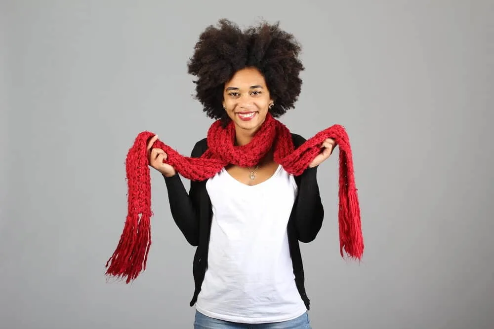 What is Coily Hair and How Do I Care for It? 2 African American female wearing black pearl earrings, a silver necklace, red scarf, white t-shirt, and a black sweater.