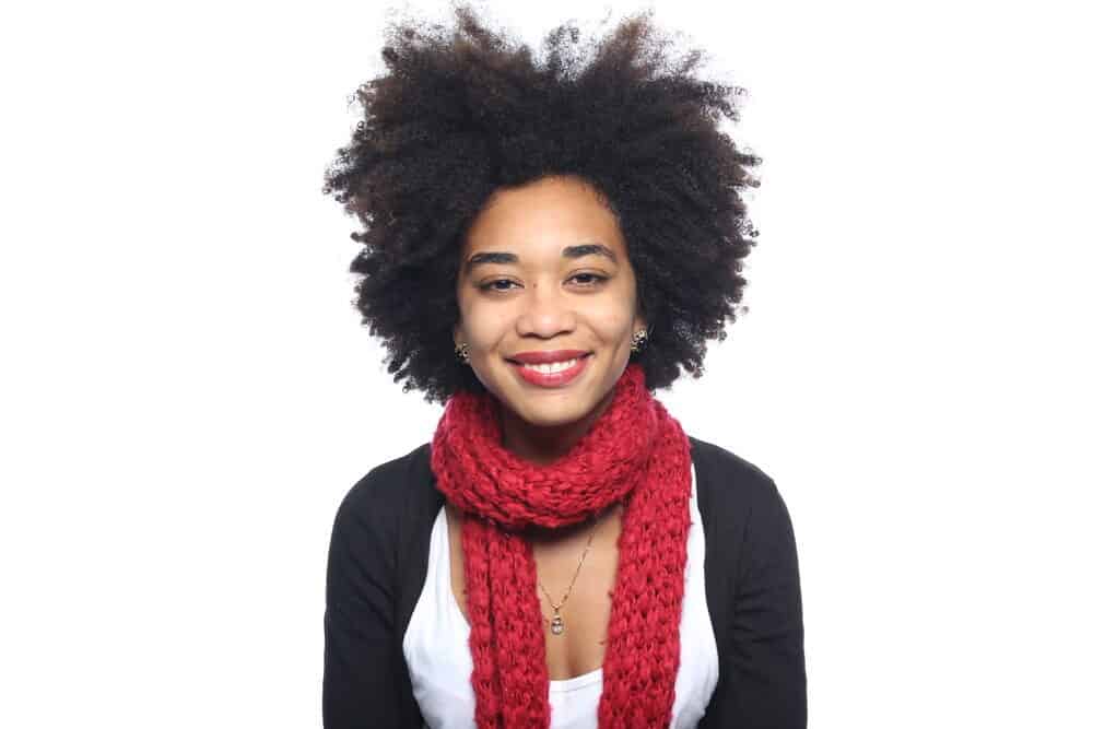African American female with 4c coily hair strands wearing black pearl earrings, a silver necklace, red scarf, white t-shirt, and a black sweater.