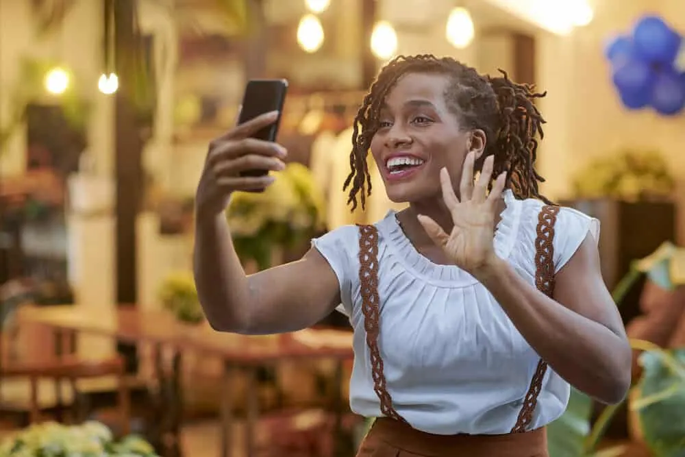 Black lady smiling while taking a photo on her cell phone.