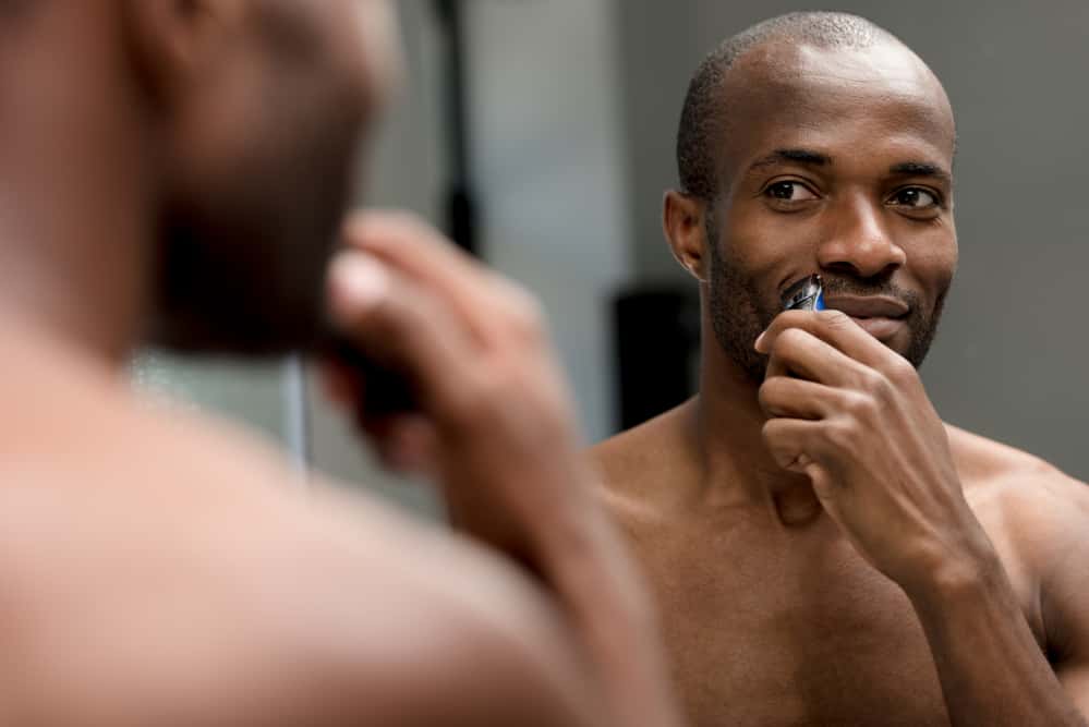 Black man with thick afro hair using cordless clippers to edge-up his mustache.