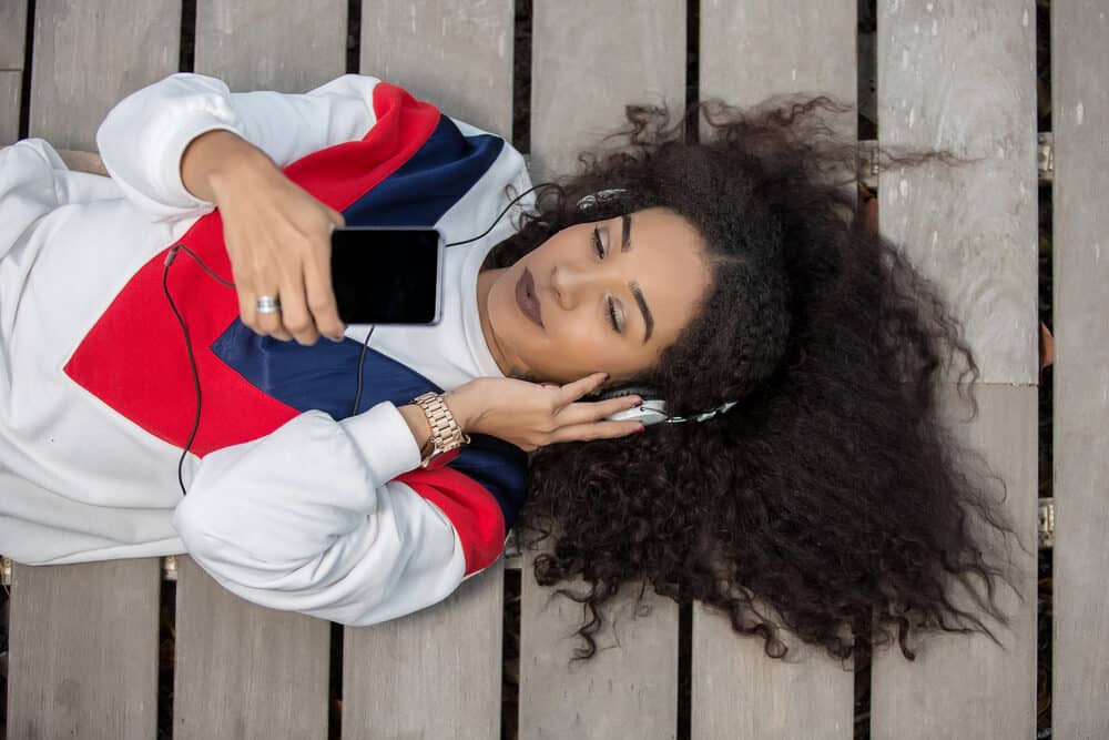 Black woman laying on the ground listening to headphones while wearing Virgin Indian hair extensions blended with her natural curl pattern.