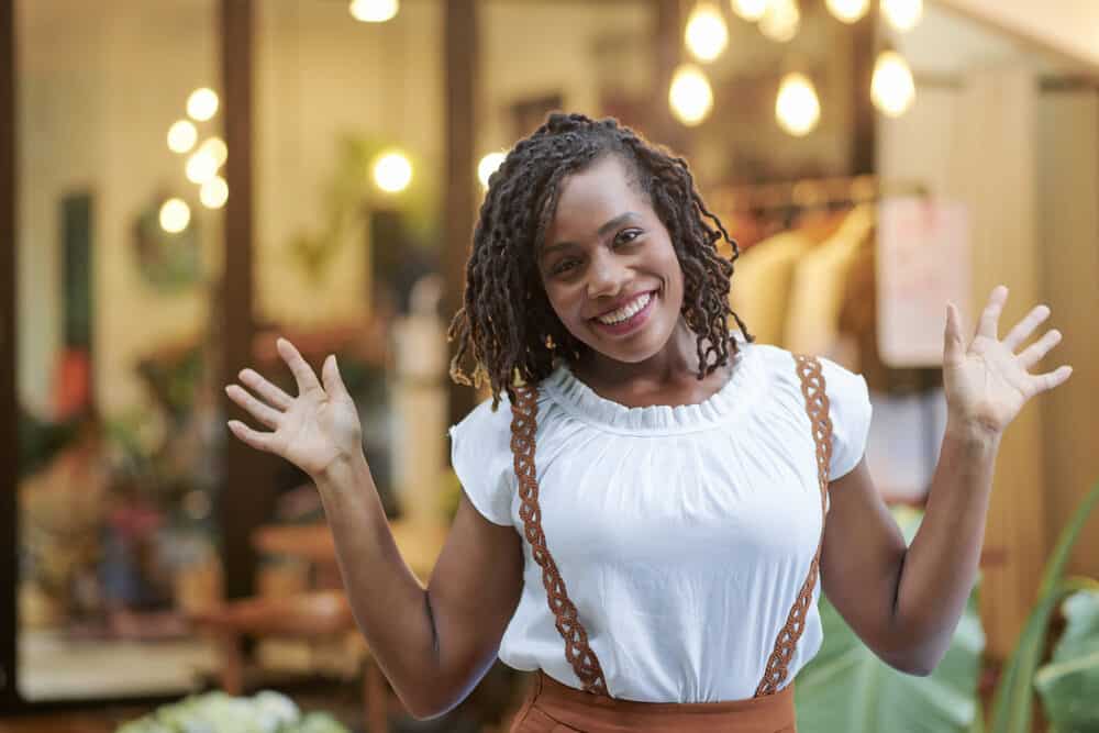 Black girl with wavy dreadlocks that look like braids, wearing a white shirt and brown dress.