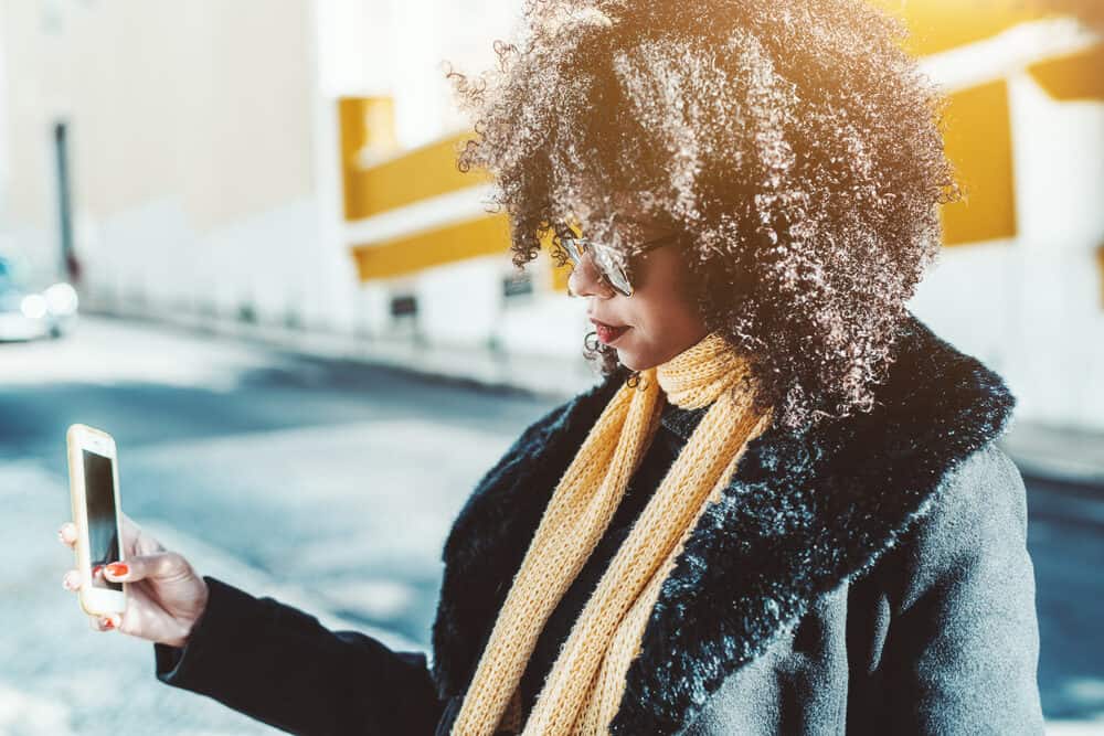 African American female talking to her hair stylist on the phone to make an appointment for hand-tied hair extensions.