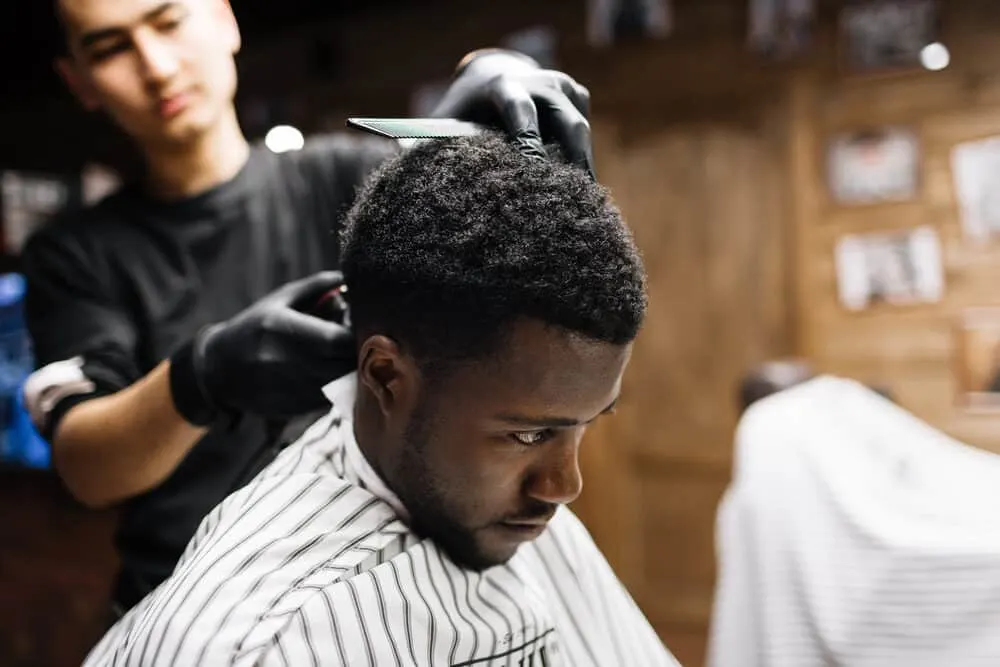 Professional barber using hair clippers to blend different lengths between the top and bottom of the customer's hair cut.