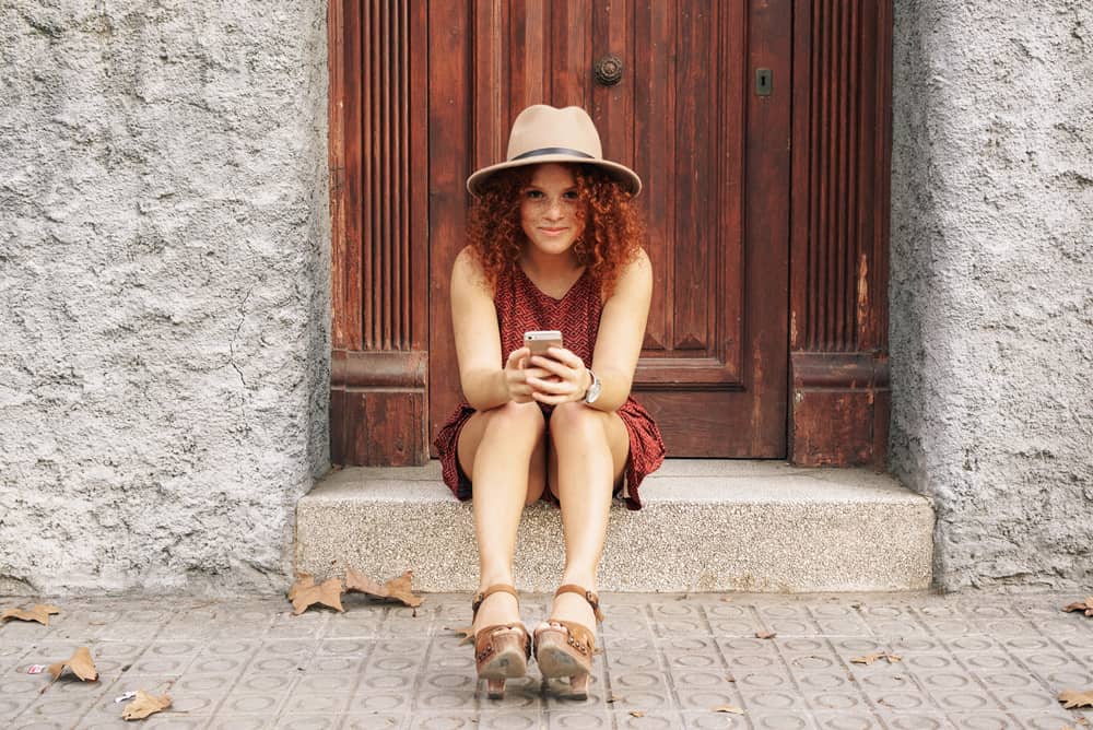 Cute girl with colored hair and freckles reading an email on her mobile phone.