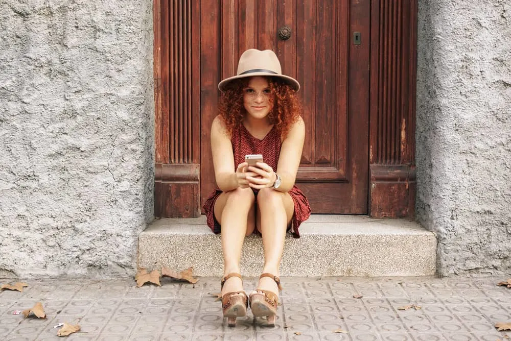 How to Neutralize Red Tones in Hair: Fix Your Hair at Home 11 Cute girl with colored hair and freckles reading an email on her mobile phone.