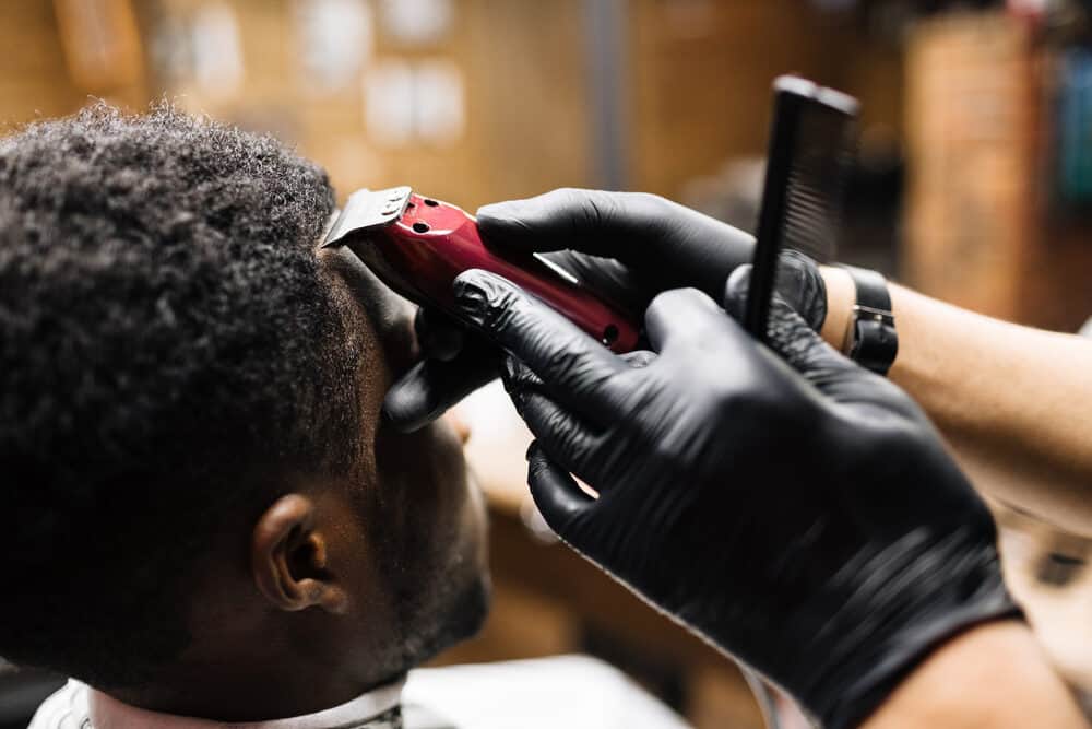 Black man getting a hair cut while the barber uses trimmers to remove hair around his hairline.