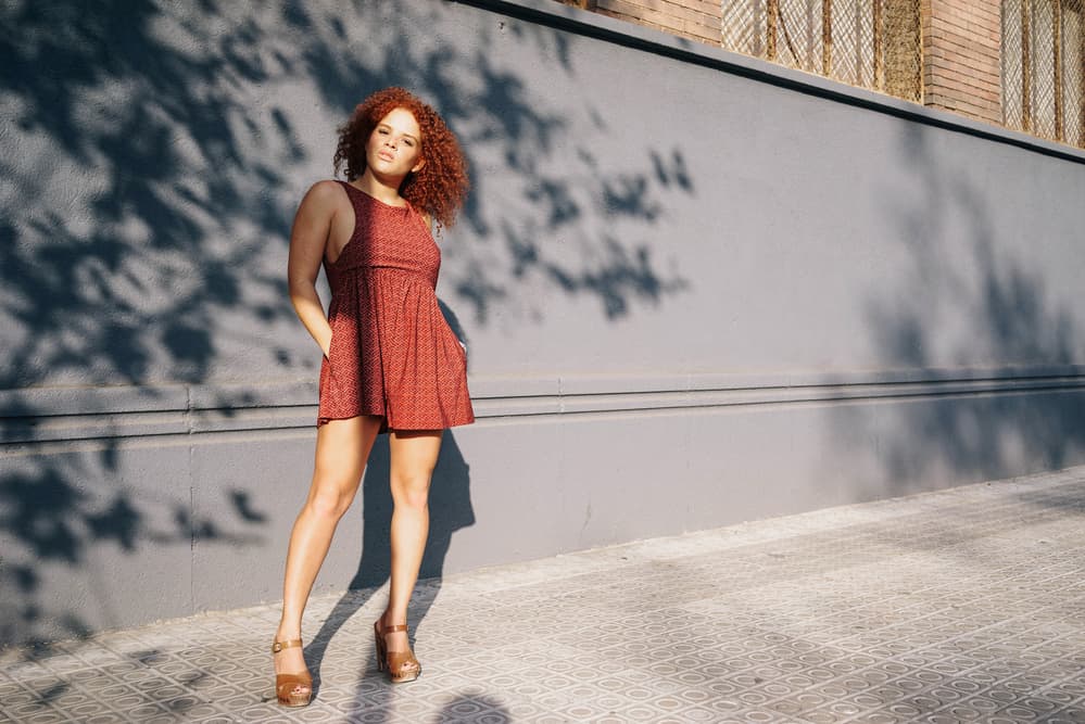 An attractive female with red streaks throughout reddish dark hair sits outside while texting with friends by mobile phone.