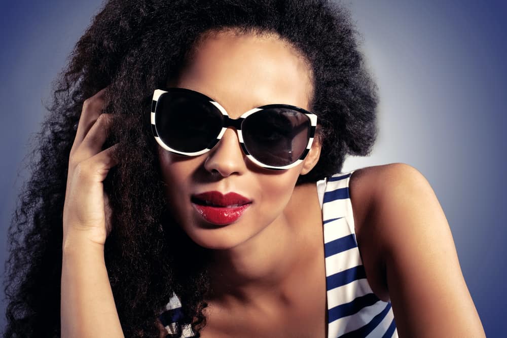  menina negra vestindo óculos de sol preto e branco, lábios vermelhos, e trança de cabelo ligado ao seu cabelo regular.