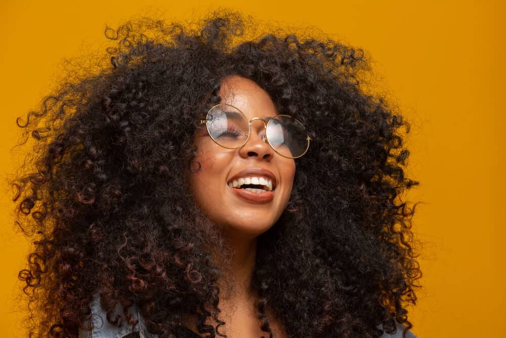 How To Choose Hair Extensions for Short Hair To Add Volume 7 Black girl wearing weft extensions lengthening super short hair while also wearing glasses, red lipstick, and a blue jean shirt.
