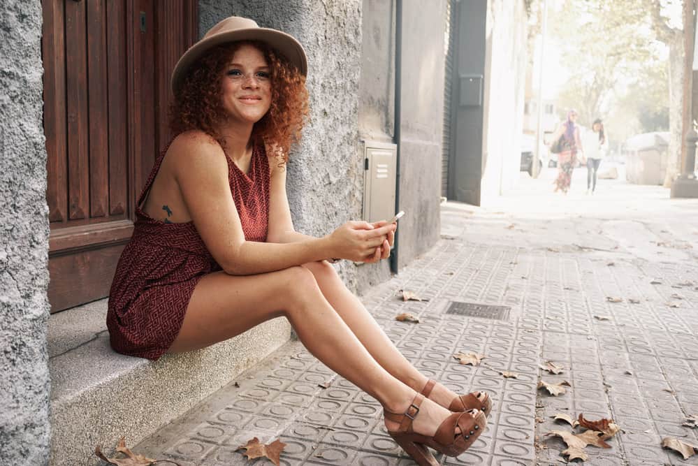 An attractive woman reading sits outside with dark brown hair with red hair tones.