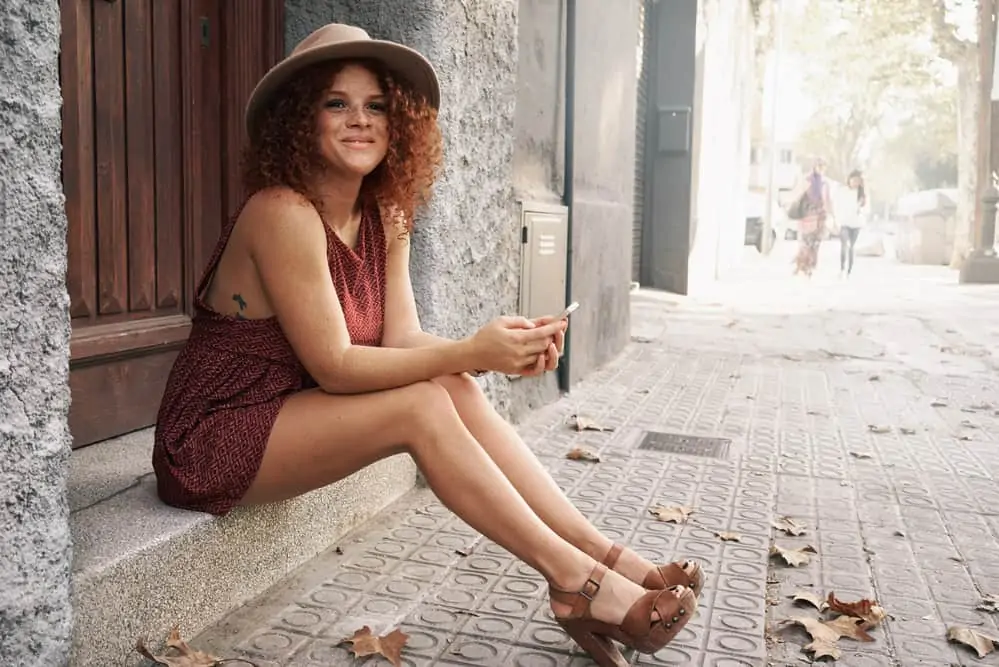 How to Neutralize Red Tones in Hair: Fix Your Hair at Home 4 An attractive woman reading sits outside with dark brown hair with red hair tones.