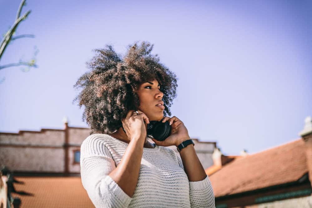 How Do Hair Extensions Work on Short, Straight, Curly, or Thinning Hair 11 A brunette walks through a park while holding headphones wearing a white sweater.