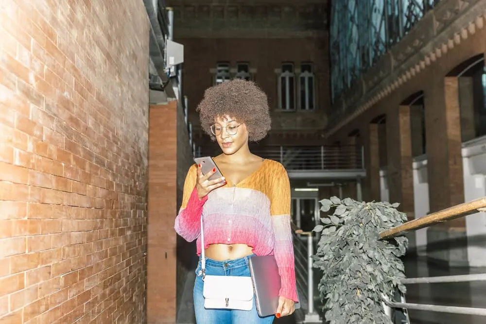 What Color Can I Dye My Black Hair Without Bleaching? Hair Dye Options for Dark Hair Colors 6 A happy African American woman with dark hair in casual clothes checks her phone inside a train station.