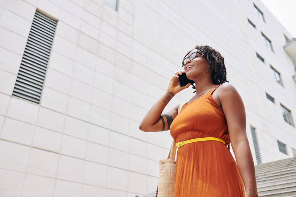 African woman with baby dreads in a city talking on the phone about how to detox dreads.