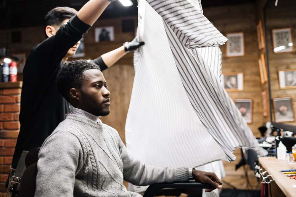 Black guy with curly hair getting a hair cut at a local barbershop.