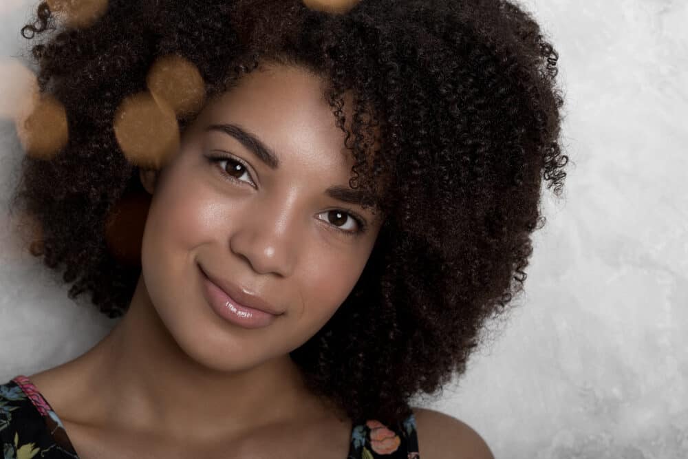 Cute black woman with a genuine smile wearing subtle make-up and pink lipstick.