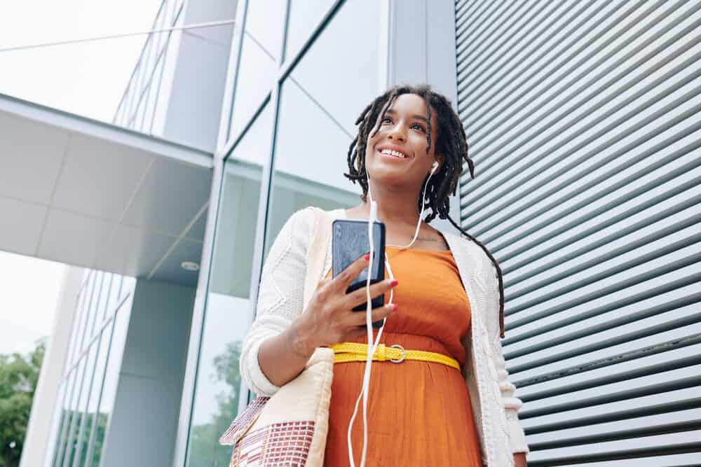 African woman wearing headphones and walking in the city listening to a podcast about natural clarifying shampoo.