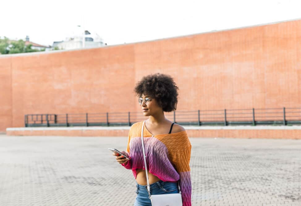 African-American girl looks at her mobile phone while wearing dark color clothes.