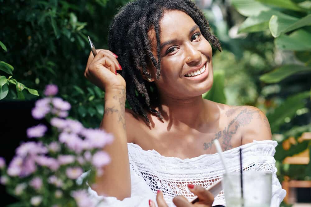 This is a picture of an African woman with a beautiful dreadlock hairstyle, smiling and relaxing outside on a summer day.