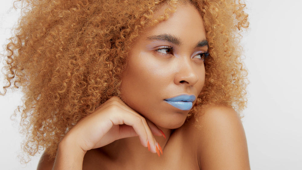Black women with medium brown hair dye, blue lipstick, and orange fingernail polish.