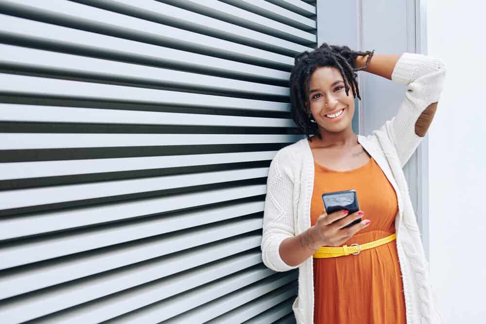 African woman on her dread journey in an orange dress standing with a mobile phone.