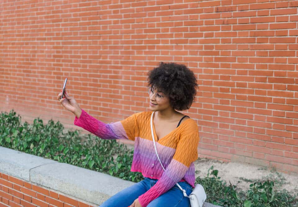 A cute girl with a hair chalk style of multiethnic background takes a selfie in front of a brick wall on a spring day.