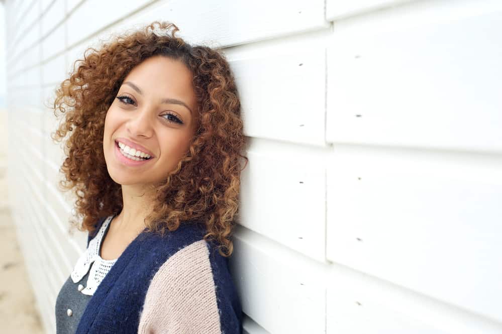 Black lady with naturally curly hair wearing balayage bob cut on with dark roots.