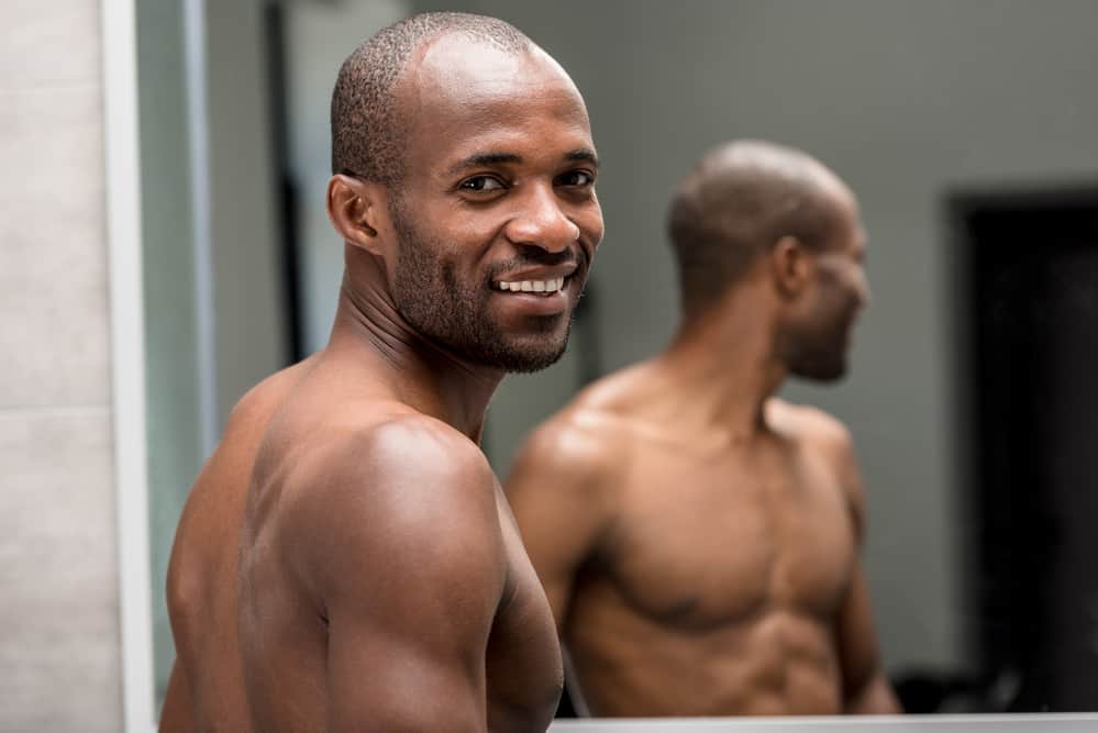 Man is looking in the mirror and smiling after shaving his black facial hair.