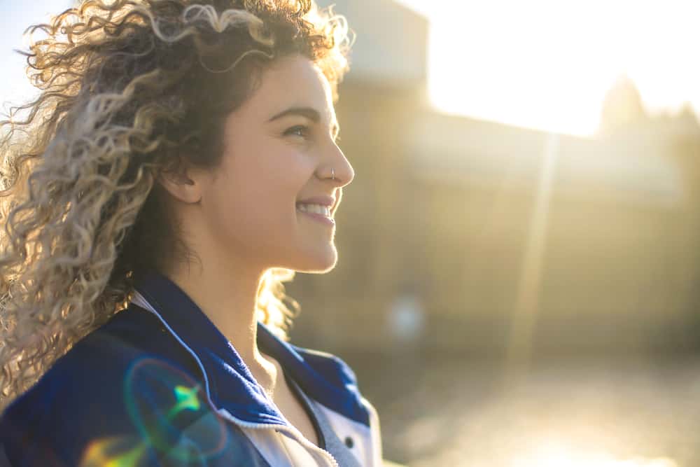  Nel mezzo di una città, c'è una splendida ragazza dai capelli biondi che cammina per strada con un anello al naso, un rossetto rosa e un grande sorriso.