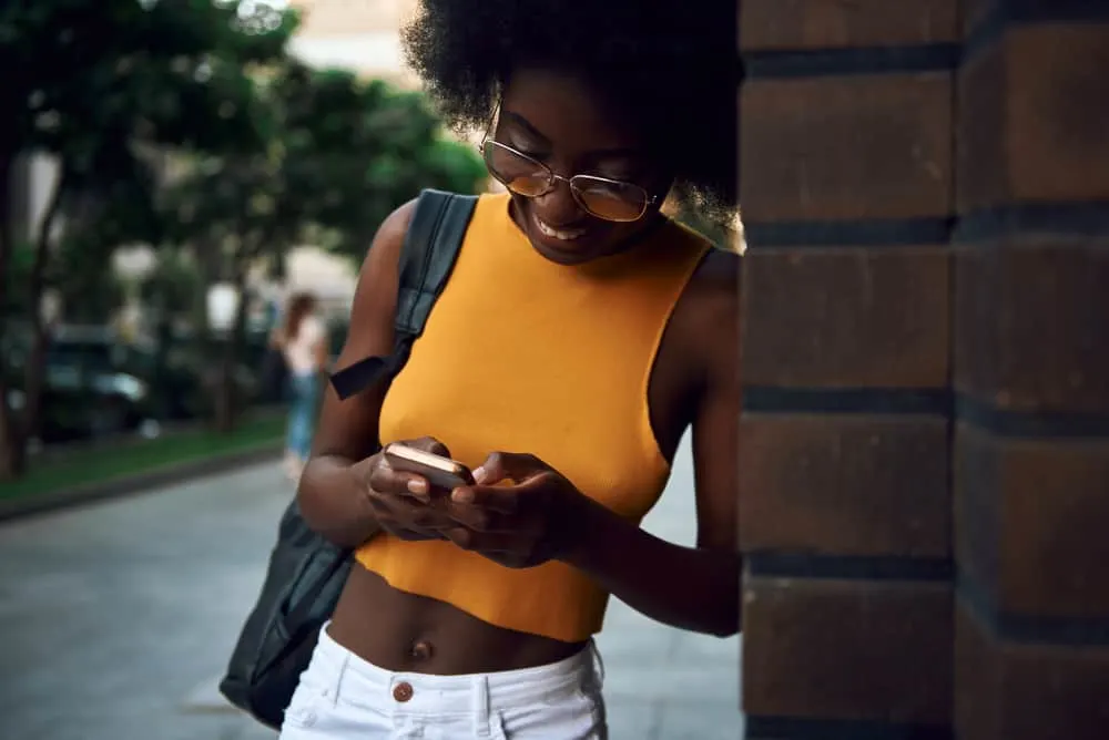 Best Blow Dryer for 4C Hair: Top Dryers for Women with Kinky Curly Natural Hair 15 Woman with black natural hair wearing glasses and standing next to a brick wall while talking on her phone.