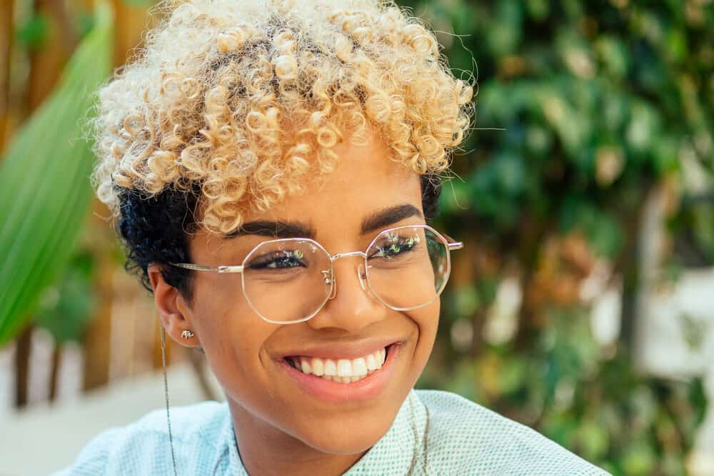 In the tropical park, a happy Afro-Latin female is seen wearing stylish eyewear and semi-permanent hair color