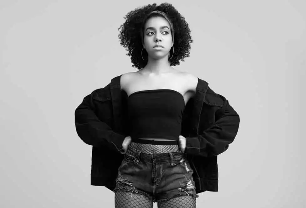 Are Hair Extensions Bad for Your Hair? How To Mitigate Damage 2 Black and white picture of a black female with clip-in hair extensions wearing a black shirt, blue jeans, and fishnet stockings.
