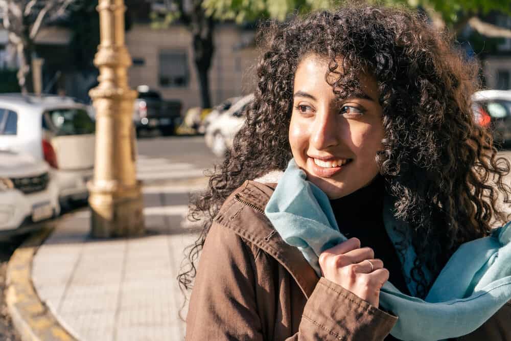 A beautiful Latin woman with curly hair strands looking into the distance while smiling