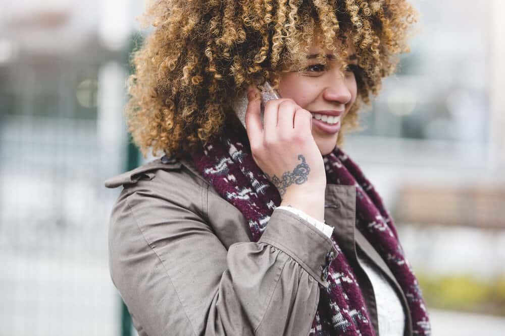 A woman is on the phone outdoors wearing a scarf during humid weather while it is foggy.