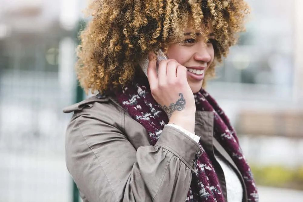 Poofy Hair: What Causes It, How To Fix It, and Prevent It 3 A woman is on the phone outdoors wearing a scarf during humid weather while it is foggy.
