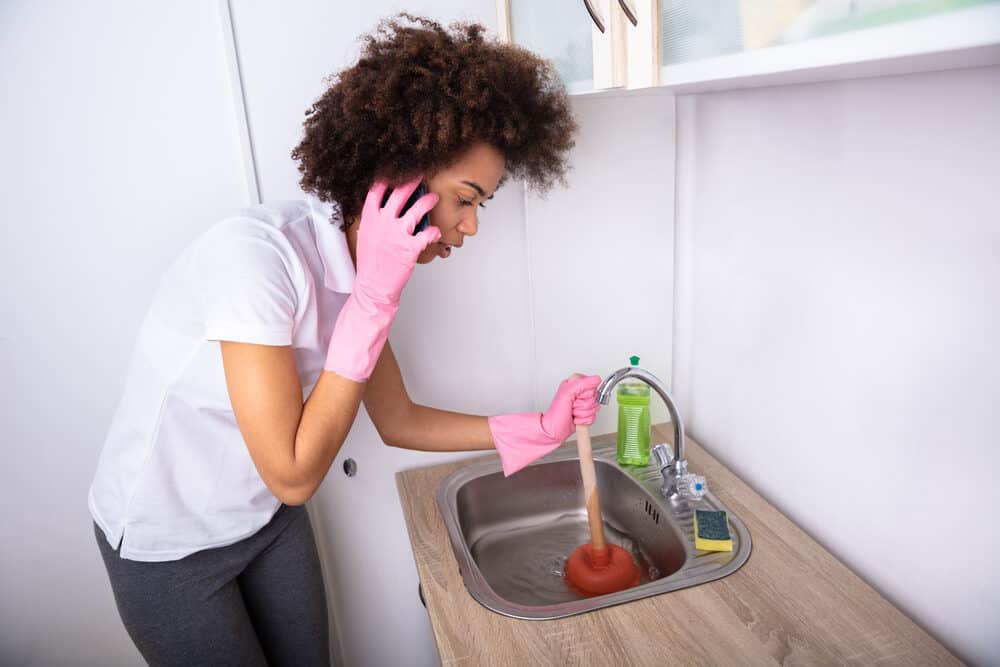 Black woman with curly hair trying to get all the hair out of a drain with cup plunger.