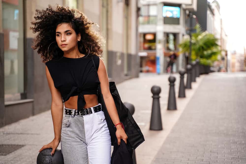 jovem colombiana com um estilo único usando brincos de argola grandes, uma camiseta preta e jeans cinza e branco.