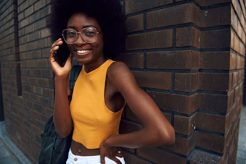 Woman in glasses standing near a brick wall and talking on her iPhone 12 to a good friend.