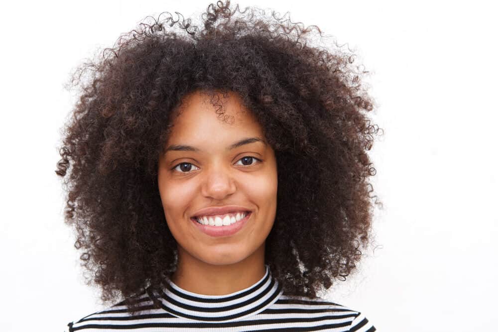 Cute black female with a curly hair cut that focuses on her oval facial structure with long layers.