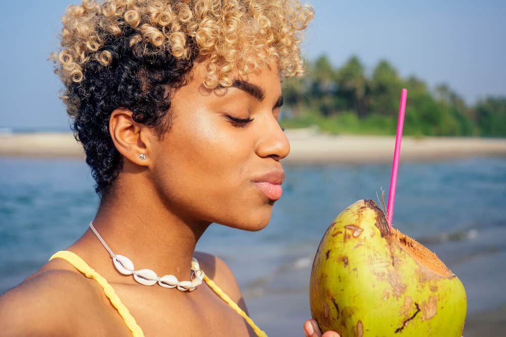 Latin female with blonde colored hair strands drinking coconut water at the beach