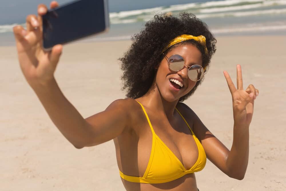 Black girl wearing a yellow bathing suit taking a selfie at the beach