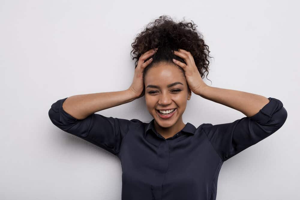 Cute black woman wearing a blue dress shirt and pink lipstick while smiling about her curly hair journey