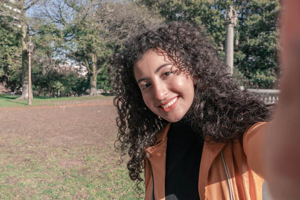 A young, attractive woman is taking a selfie at a public park with a generous layer of makeup